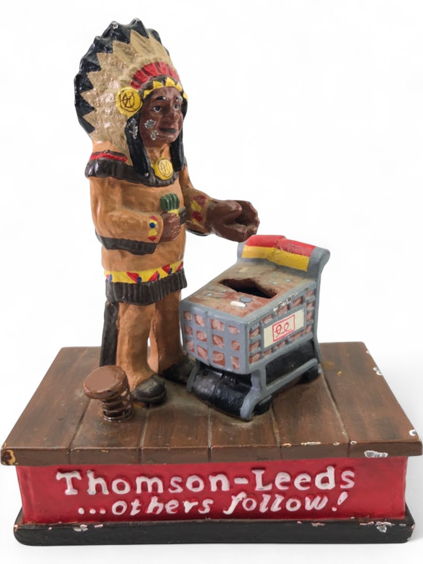Thomson-Leeds Native American Mechanical Coin Bank: Vintage cast iron mechanical coin bank by Thomson-Leeds Company, Inc. Depicts a Native American figure placing coins into a shopping cart. Features painted finish showing wear, chips, and rust. Text o