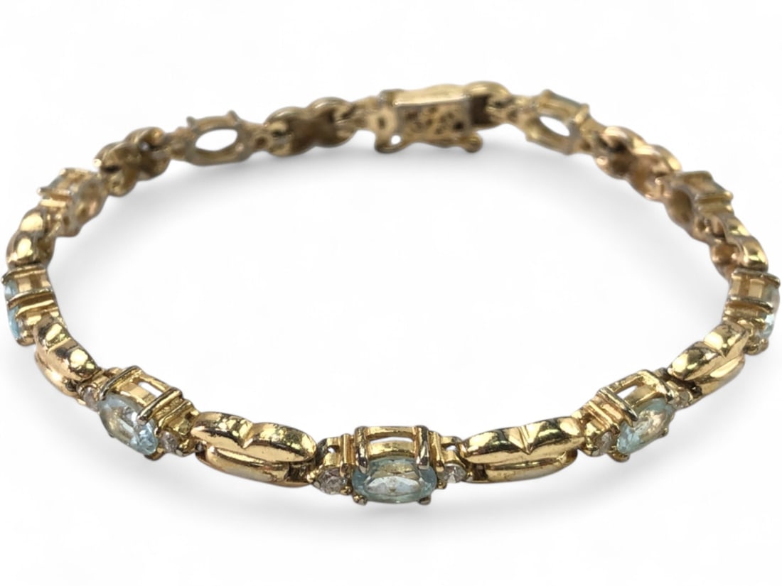 Sterling Gold-Plated Blue Gemstone Bracelet 7.5": Sterling silver gold-plated link bracelet featuring oval-cut blue gemstones, likely topaz, flanked by small clear accent stones. Each stone is prong-set within decorative links. Secured with a box cla
