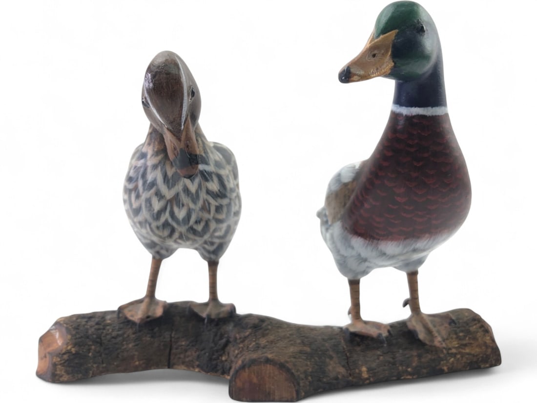 Hand Carved and Painted Mallard Drake and Hen: Pair of hand-carved and painted wooden mallard ducks, including a drake and a hen, mounted on a natural wood branch base. The figures feature detailed feather painting and glass eyes. Unmarked. 6"h.