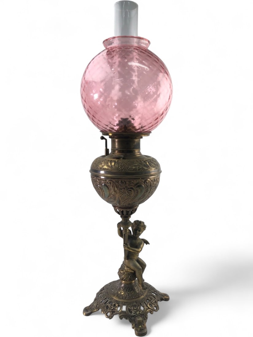Bradley & Hubbard Cherub Brass Oil Lamp: Victorian era oil lamp by Bradley & Hubbard featuring a cast brass base with a winged cherub figure seated on a rocky mound. The lamp includes a pink diamond-quilted glass globe and a clear glass chim