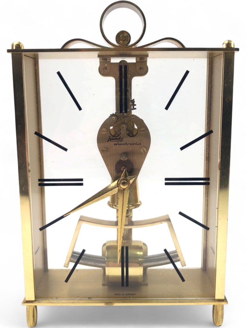 Kundo Electronic Brass Skeleton Clock: Kundo electronic skeleton clock, manufactured by Kieninger & Obersfell. Features a brass frame with glass panels, a floating dial with black baton hour markers, and a visible electromagnetic pendulum 