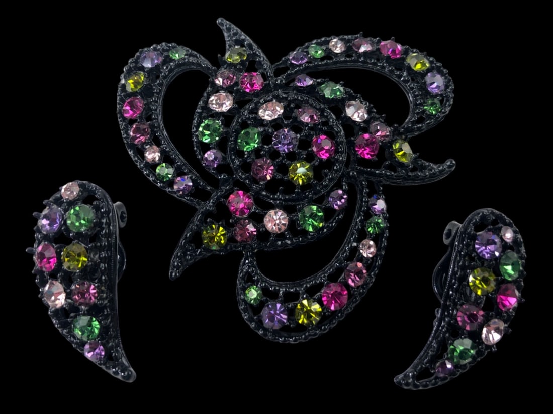 Vintage Black Japanned Rhinestone Brooch & Earrings: A vintage jewelry set featuring a large openwork brooch and matching clip-on earrings. The pieces are constructed from black japanned metal set with multi-colored round-cut rhinestones in shades of pi