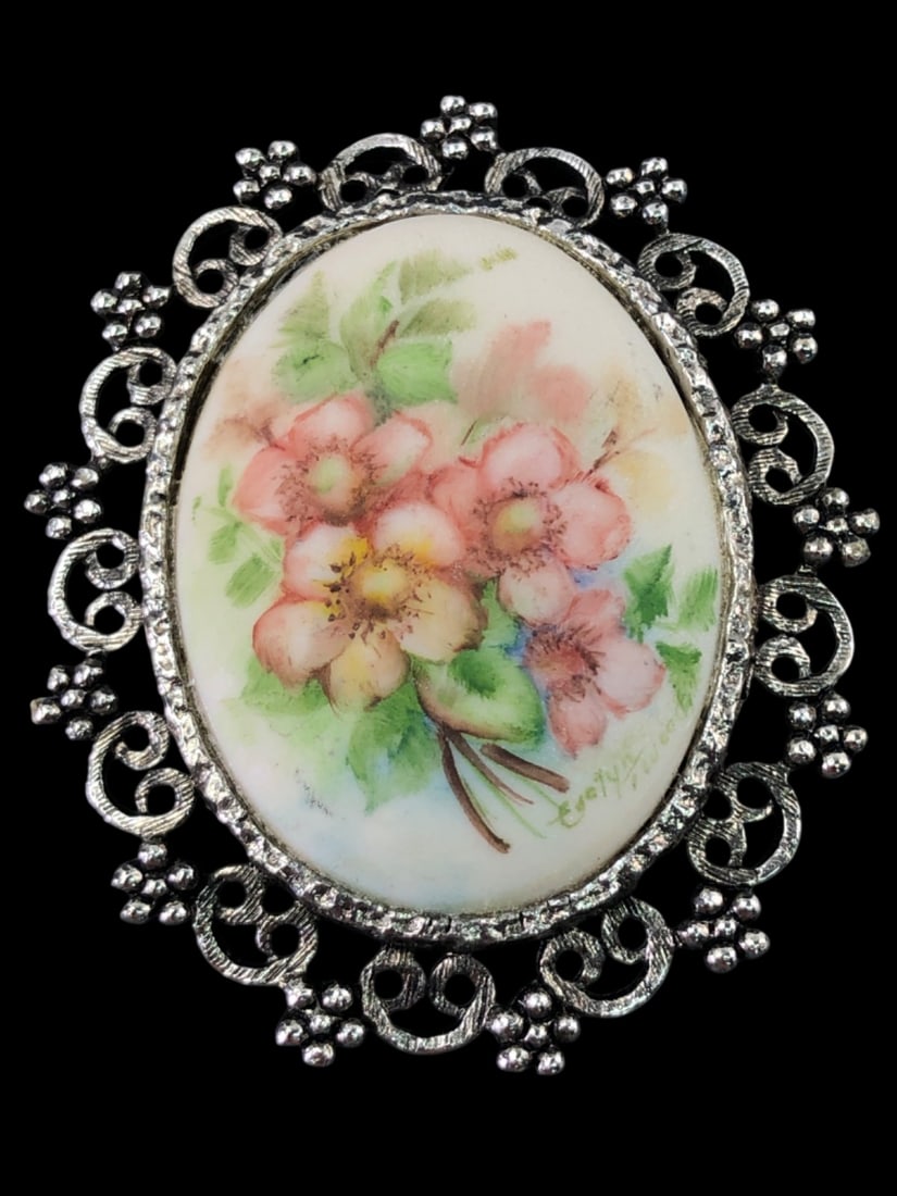 VTG Evelyn Signed Floral Brooch: Vintage oval brooch featuring a hand-painted floral motif on a porcelain cabochon. The artwork depicts pink and yellow wild roses with green foliage, signed "Evelyn ?" in the lower right. Set in a sil