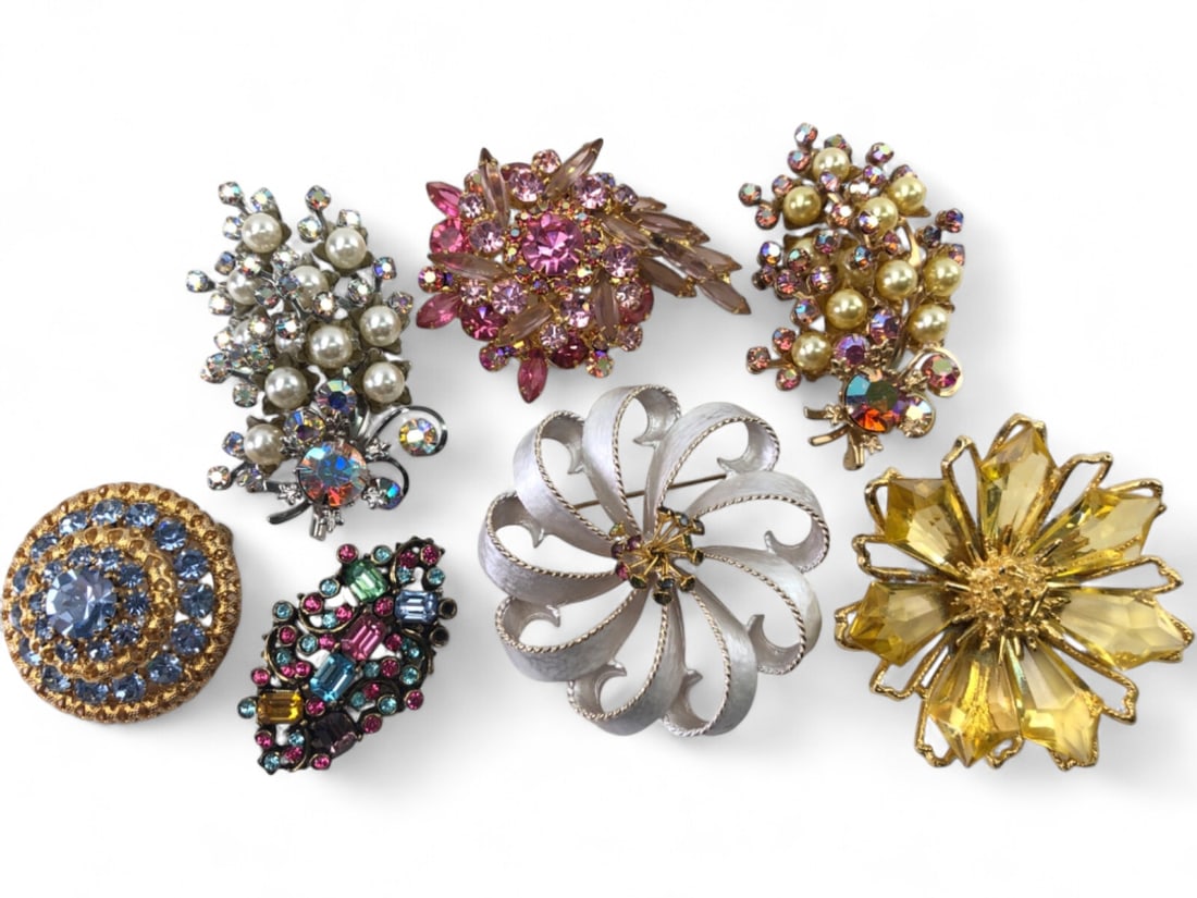 VTG Costume Jewelry Brooch Lot of 7: Lot of seven vintage costume jewelry brooches. Includes a large yellow faceted glass flower, a silver-tone textured ribbon spray with multi-color rhinestones, a gold-tone tiered blue rhinestone circul