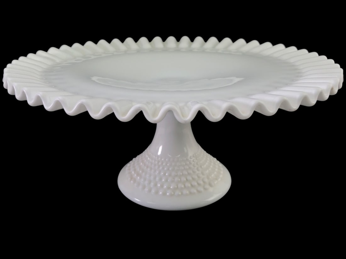 VTG Fenton White Milk Glass Hobnail Cake Stand: Vintage milk glass cake stand attributed to Fenton. Features a ruffled rim and a hobnail pattern on the underside of the plate and the pedestal base. Unmarked. 12.25" dia. Shows minor surface wear and