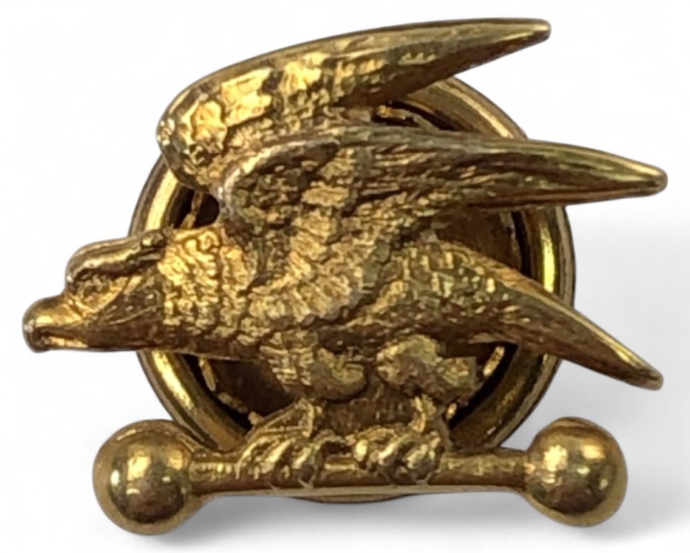 10K Gold Eagle on Bar Lapel Pin: 10K gold lapel pin featuring an eagle perched on a horizontal bar with ball ends. Features a screw-back closure. Stamped "10K" on the reverse. Measures 0.5" wide. Weighs 0.96 grams.
