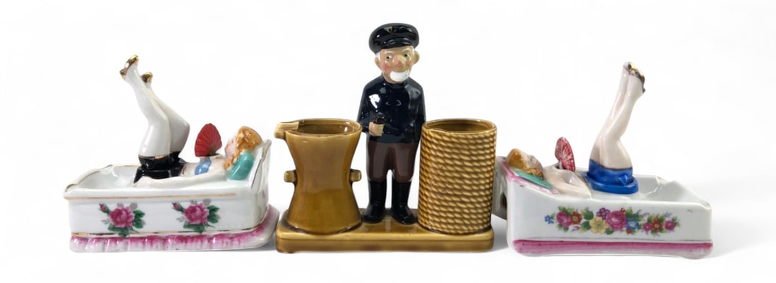 Hand-Painted Porcelain Risqué Ashtrays and Holder: Set of three hand-painted porcelain novelty items including two risqué ashtrays featuring reclining women with movable legs and a nautical-themed holder depicting a sea captain with a pipe standing