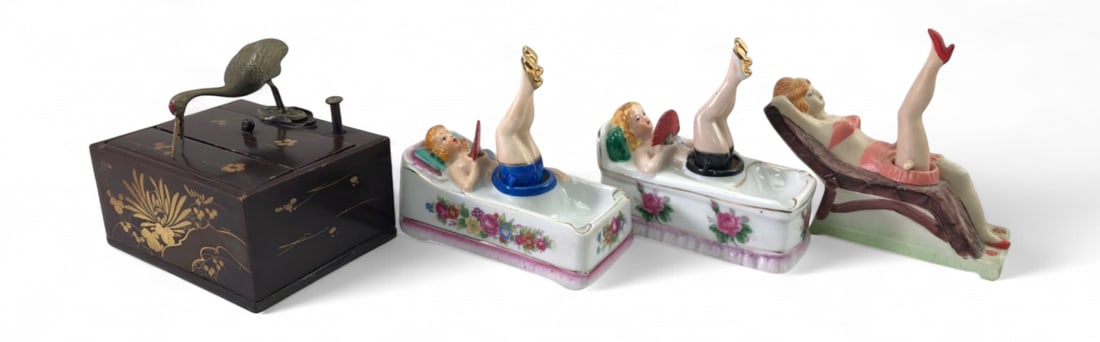 Japanese Lacquer Cigarette Box and Porcelain Ashtrays: Lot includes a Japanese black lacquer cigarette box with a mechanical brass crane dispenser (needs fixing) and three hand-painted porcelain pin-up girl ashtrays. The lacquer box features gilt floral