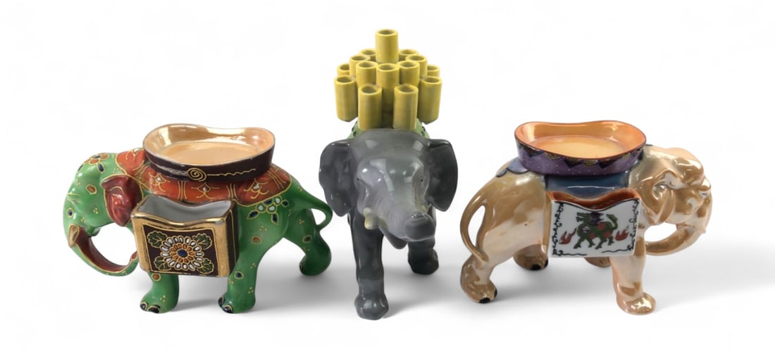 Hand-Painted Ceramic Elephant Match and Cigarette Holders: Set of three hand-painted ceramic elephant figurines. Includes two match holders with side-mounted panniers and top wells, one green with floral motifs and one iridescent lustre with a dragon design.