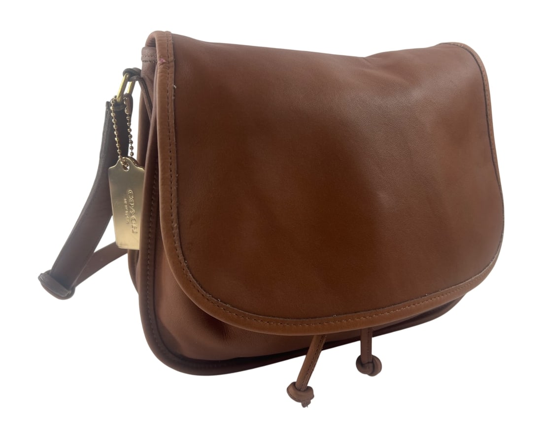 Coach Leather Drawstring Flap Shoulder Bag: Coach shoulder bag crafted from brown glove-tanned cowhide leather. Features a front flap closure over a drawstring main compartment, an interior zippered pocket, and an adjustable shoulder strap.