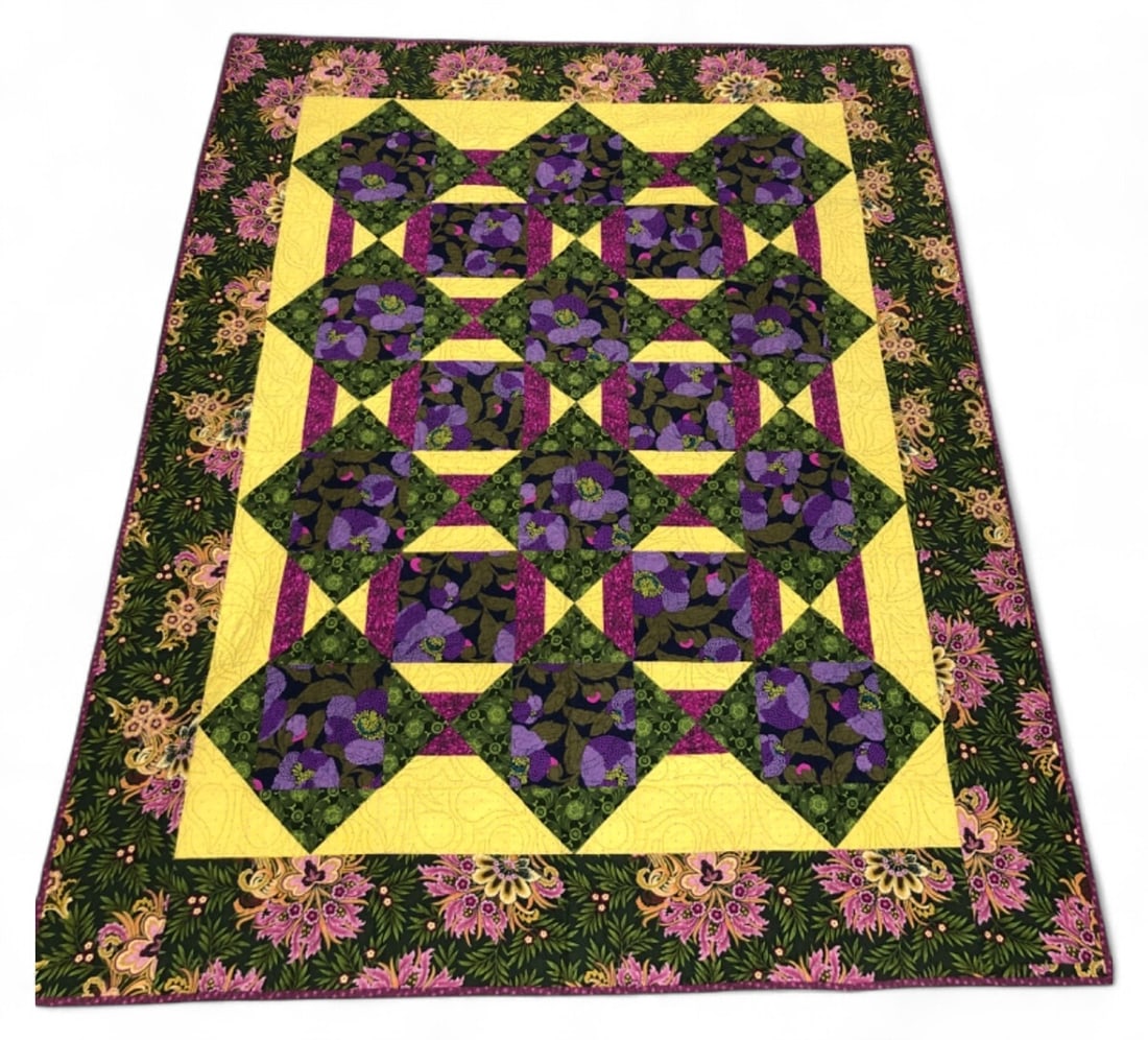 Handmade Floral Patchwork Quilt: Handmade cotton patchwork quilt featuring a vibrant floral design in purple, magenta, mustard yellow, and olive green. The piece is constructed with geometric blocks and a wide floral border. The reve