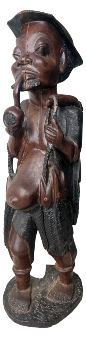 African Carved Wood Figure with Pipe & Fish 25H: Large carved wood figure of a man wearing a hat and smoking a pipe, carrying fish and pouches. Originating from regions like Zimbabwe or Malawi, mid-20th century. Unmarked solid wood construction.