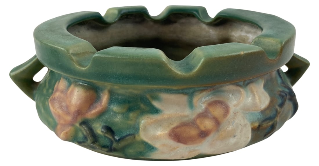 Roseville Pottery Magnolia Ashtray 28: Vintage Roseville Pottery ceramic ashtray in the Magnolia pattern, shape number 28. Features a green matte glaze with molded pink and white blossoms and dual side handles. Base is incised "Roseville