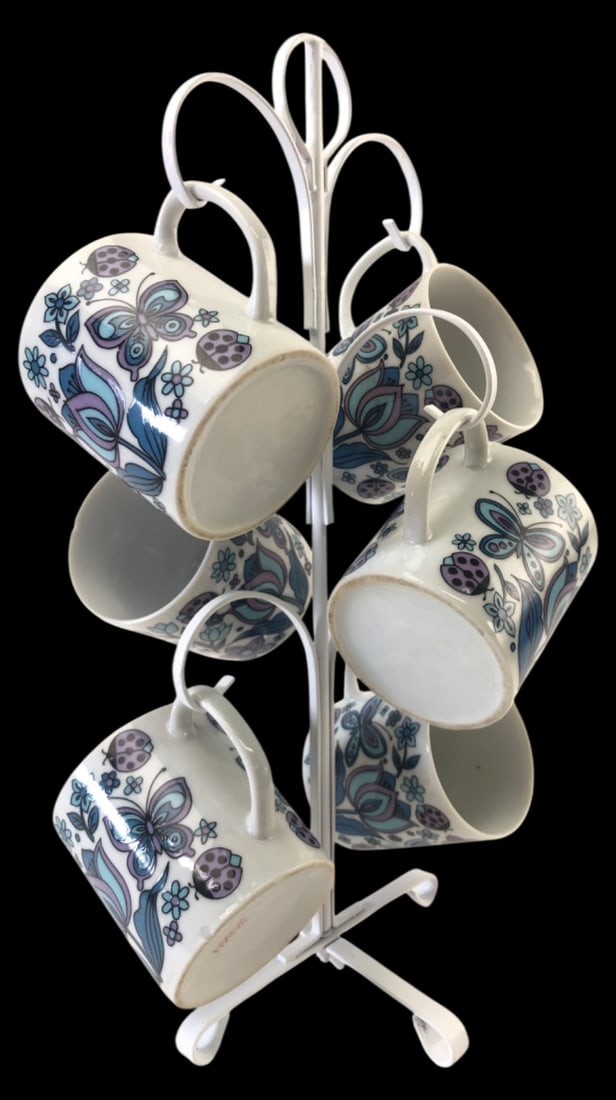 VTG Japan Floral Butterfly Mugs & Stand: Set of 6 vintage ceramic mugs with a white metal tree stand. Made in Japan. Features a retro blue and purple floral, butterfly, and ladybug motif. Mugs measure 3" H. Marked "JAPAN" on base.
