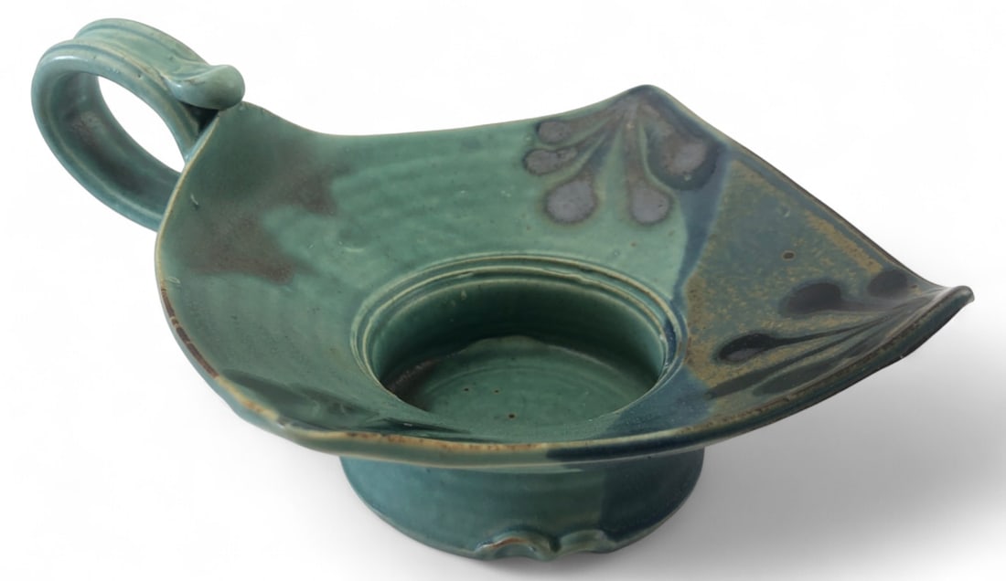 Otis Pottery Signed Handled Candle Holder: Art pottery handled candle holder by Otis Pottery of East Jordan, MI. Features a green glaze with dark floral corner motifs and a central candle well. Signed on the unglazed base. Measures 8.5" wide