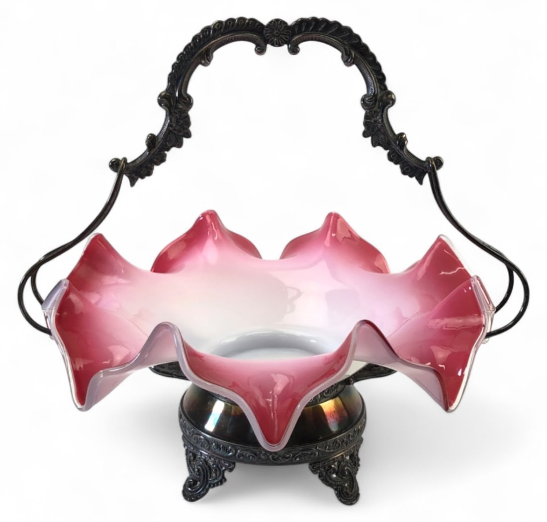 Aurora Silverplate Bride's Basket Art Glass Bowl: Victorian style bride's basket featuring an 11" diameter ruffled pink to white art glass bowl. It rests in an 11" H ornate silverplate handled holder by Aurora Silver Plate Mfg Co. Holder features flo