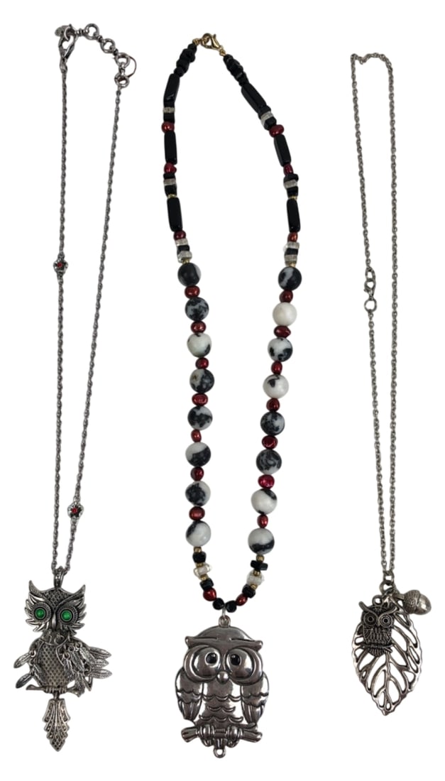 Three Silver-Tone Owl Pendant Necklaces: Collection of three unmarked silver-tone owl pendant necklaces. Includes an articulated owl with green eyes and dangling feathers, a solid owl pendant on a beaded chain with black, white, and red
