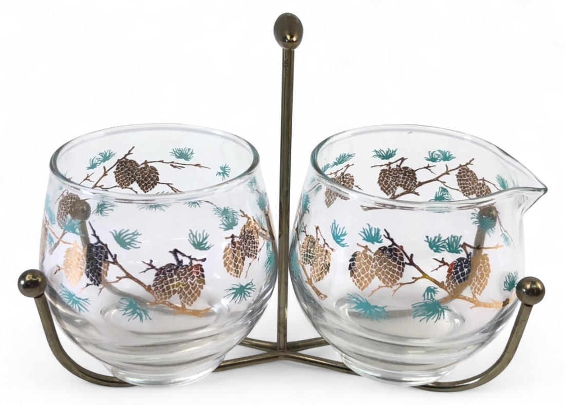 Libbey Pinecone Cream & Sugar Set w/ Caddy: Libbey glass cream and sugar set in a brass-toned metal caddy. Features a mid-century pinecone and pine needle motif in brown, gold, and teal. Includes a creamer with spout and an open sugar bowl. Gla