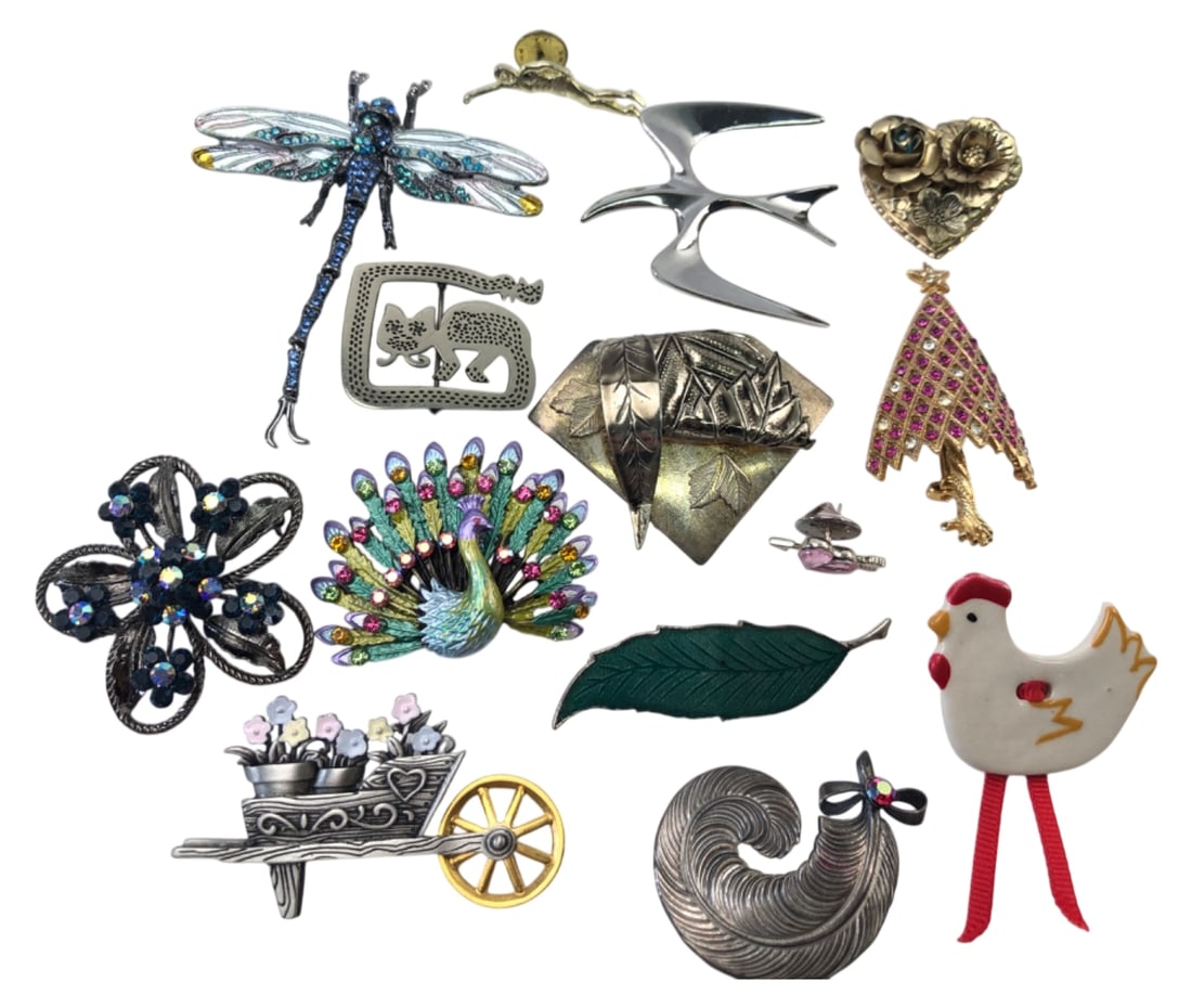 JJ & Assorted Costume Jewelry Brooch Lot: Lot of 14 costume jewelry brooches. Includes a wheelbarrow pin marked JJ (Jonette Jewelry), a large rhinestone dragonfly, an enameled peacock, a rhinestone Christmas tree, a ceramic chicken, and