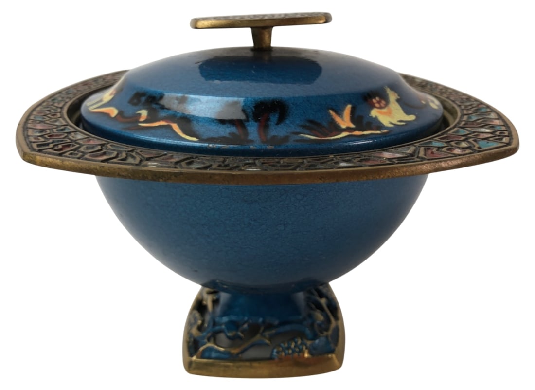Blue Enamel & Brass Lidded Bowl Camel Motif: Blue enamel and brass lidded pedestal bowl featuring a camel and figure motif on the lid. Designed with a geometric champlevé style enameled rim and finial, resting on a pierced brass base. Unmarked.