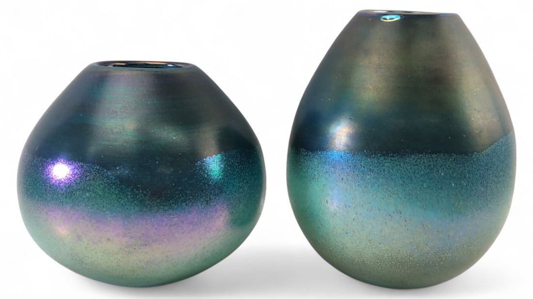 Carolyn Kinder Iridescent Arian Art Glass Vases: Pair of iridescent studio art glass vases. Features a smooth dark teal upper half transitioning to a textured, speckled lighter blue-green lower half with purple highlights. Polished pontil bases