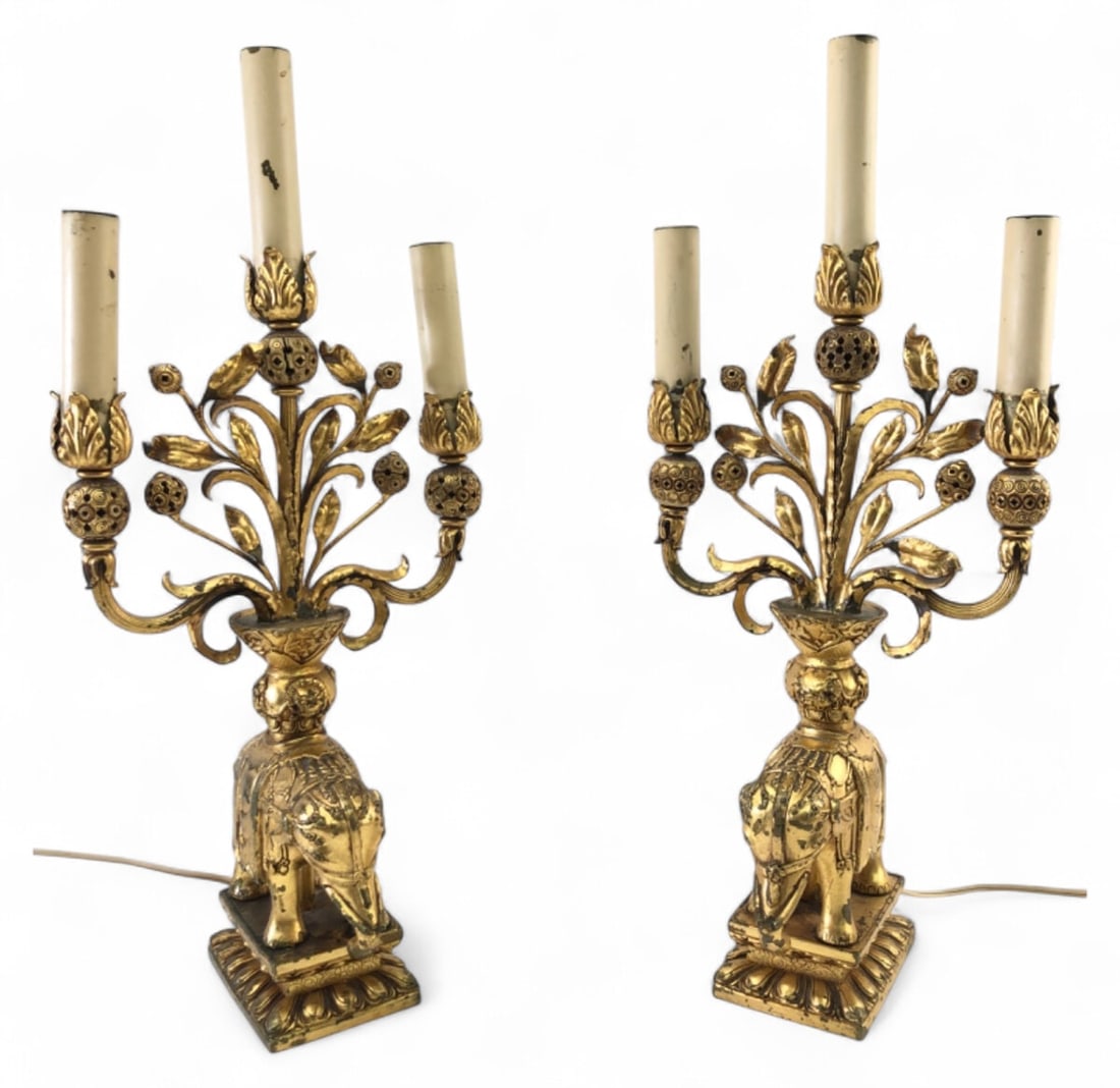 Pair Chinoiserie Gilt Elephant Candelabra Lamps: Pair of Chinoiserie-style candelabra lamps featuring intricate gilt cast metal elephant bases. Each lamp has three candle-style lights with foliate arms. 17.5" H. Condition: Untested. Shows wear to
