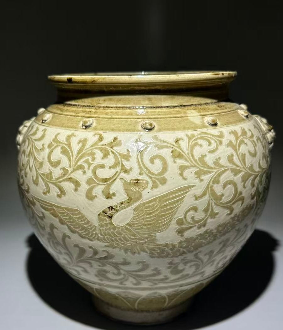 Jin 12th C Celadon Phoenix Peony Mask-Handle Jar: Jin Dynasty, 12th century, A celadon-glazed carved jar with phoenix and peony decoration and mask handles with bosses, finely carved and well-balanced / Height 23 cm / Belly Diameter 21 cm/ AI Authent