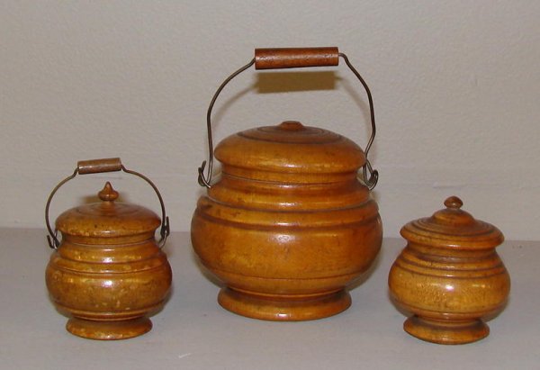 THREE PEASEWARE JARS. Turned wooden jars with lids.: THREE PEASEWARE JARS. Turned wooden jars with lids. Two have wire bale handles. All have varnish finish with varying degrees of wear. The largest is missing a finial. 3 1/8"d. 3 1/2"h., 3"d. 2 1/2"h.,