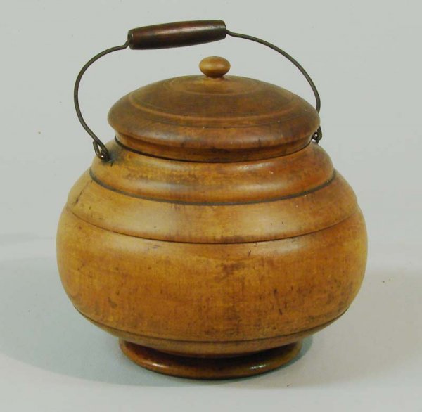 MEDIUM PEASEWARE COVERED JAR.: American, 19th Century. Turned maple jar with a wire bale handle; the lid has a flattened ball finial. Illegible signature on the underside. Retains an older finish. 6 1/2"h.