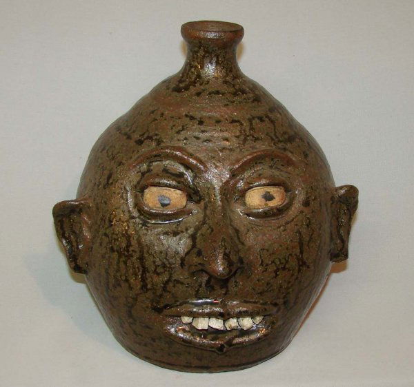 LANIER MEADERS GROTESQUE JUG. Redware face jug wit: LANIER MEADERS GROTESQUE JUG. Redware face jug with dark green ash glaze and stone teeth. Applied handle. Incised script signature Lanier Meaders" (1917-1998, member of the famous family of potters, W