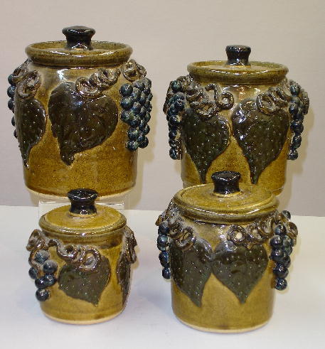 RARE GRADUATED SET OF FOUR LANIER MEADERS COVERED J: RARE GRADUATED SET OF FOUR LANIER MEADERS COVERED JARS. All have incised signatures on the bottom with an olive green glaze. Applied dark green leaves and vines with blue grapes. Only one other set kn