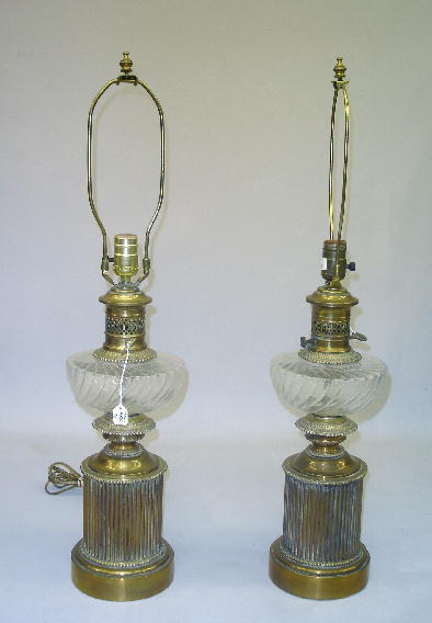 PAIR OF BRASS TABLE LAMPS. Round stepped bases hav: PAIR OF BRASS TABLE LAMPS. Round stepped bases have ribbed sides and a clear pressed glass font resembling oil lamps. Variations to piercings around the faux burners. Includes harps for shades. 29 1/4