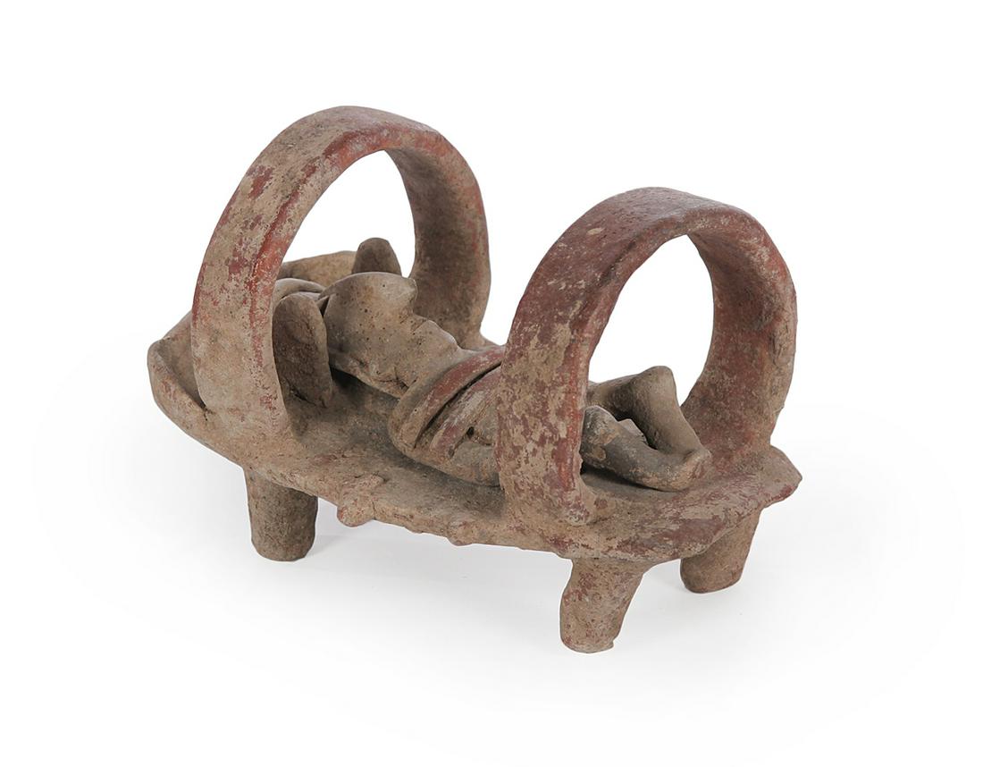 PRE-COLUMBIAN POTTERY FIGURE.: Colima, ca 300 BC- 300 AD. Male reclining figure with elaborate headdress on a separate bier or other platform with circular straps. 6"h. 8"l. Ex Artemis Gallery, ex Roy Oswald Collection (Arizona).