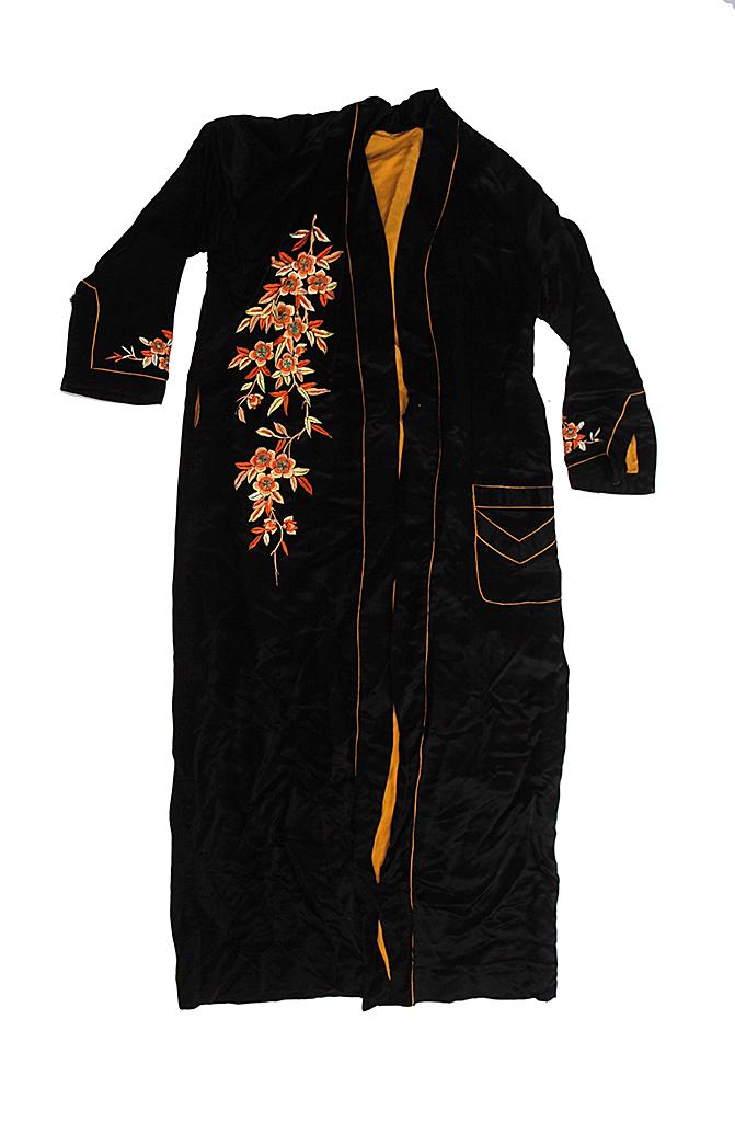 TWO PIECES OF CLOTHING IN TAILOR'S CASE.: Mid 20th century. Man's Asian black silk robe with orange floral embroidery and gold lining. 55"l. And a woman"s Cuban pale pink dress with hand painted red roses. "Creaciones Campana de Oro, Hecho en