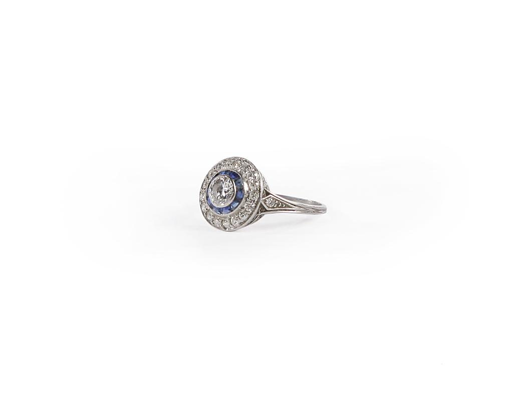 ART-DECO PLATINUM DIAMOND AND SAPPHIRE CLUSTER RING.: American, 2nd qtr.-20th century. Art deco platinum ring (tested with x-ray metal tester) set with central old European cut diamond, slightly out of round, approx. .42ct., in a border of calibre cut bl