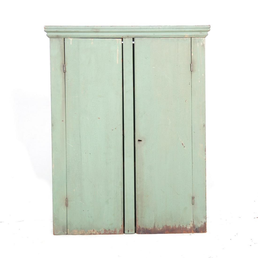 HANGING CUPBOARD.: American, 3rd quarter 19th century, mixed woods. Old worn apple green paint, molded cornice, single board doors with center stile and three added interior shelves. 36"h. 28.5"w. 55."d.