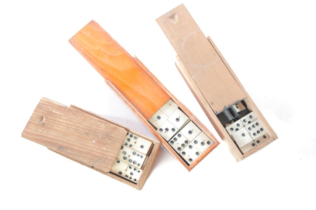 THREE SETS OF AMERICAN BONE DOMINOES.: Late 19th century. Bone and ebony with brass pegs. Two sets of twenty eight (one with splits and chips) and one set of fifty four. In sliding lid wood boxes.