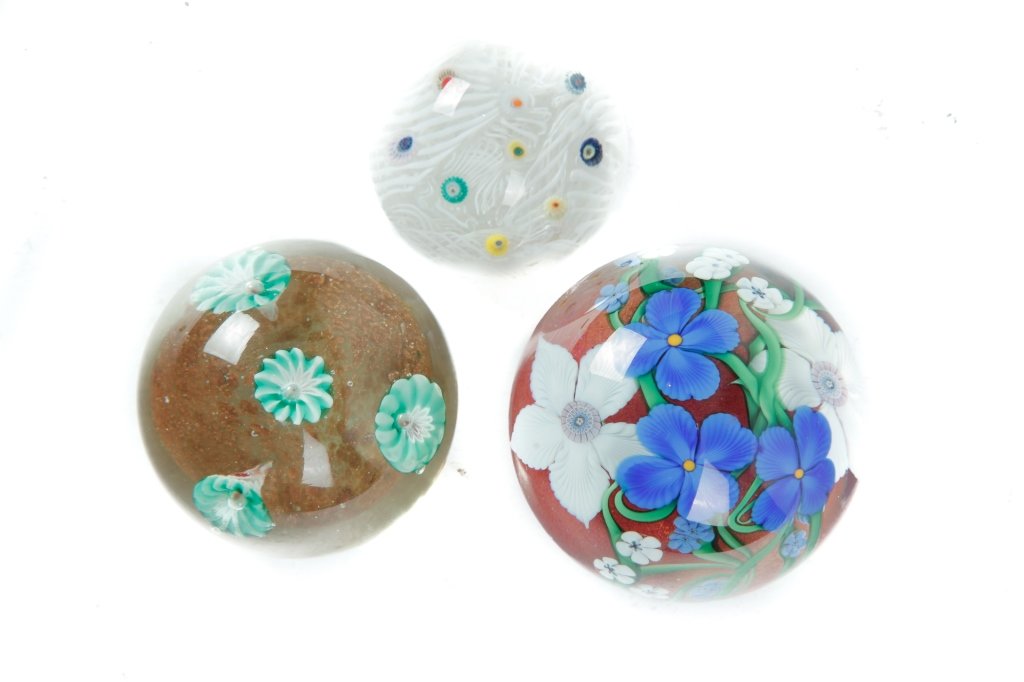 THREE ART GLASS PAPERWEIGHTS.: 20th century. Orient and Flume, dated 1983 with white and blue flowers, green vining, and orange mica background, 3"h. 3"dia. Strathern with multicolored cones and white latticino, 2"h. 2.5"dia. And g