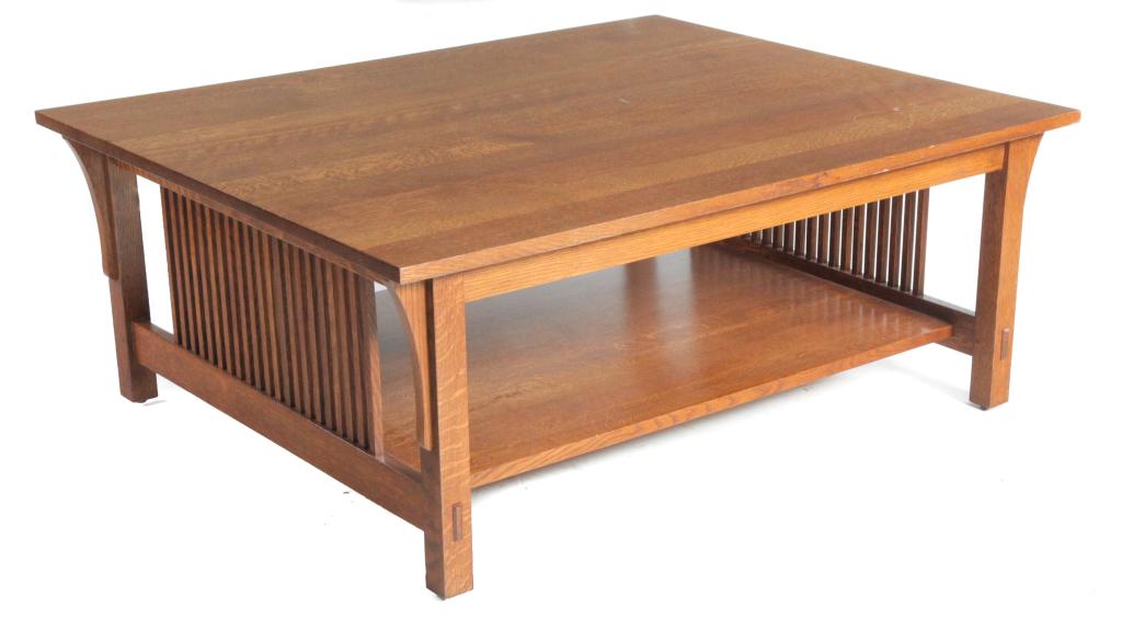 STICKLEY ARTS AND CRAFTS STYLE COFFEE TABLE.: American, late 20th century. Quarter sawn oak, slat sides, mortised construction, lower shelf, and square legs with applied decoration. Branded label. 17"h. 44"w. 36"d.