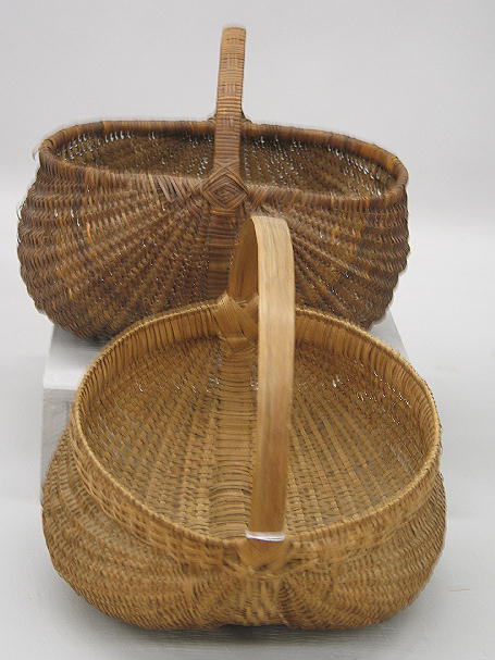 TWO BUTTOCKS BASKETS. Both in a dry natural brown: TWO BUTTOCKS BASKETS. Both in a dry natural brown color. The woven splint example shown has thirty-two ribs. 11"w. 11"h. Other is made of woven splint and caning with Eye of God designs on the handles