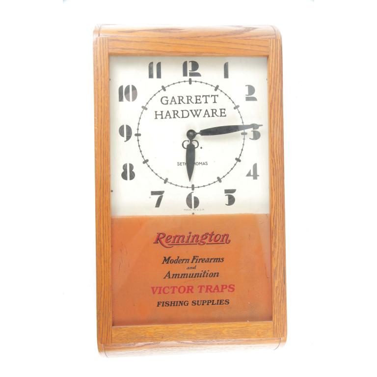 GARRETT HARDWARE REMINGTON ADVERTISING CLOCK: GARRETT HARDWARE REMINGTON ADVERTISING CLOCK. American, 20th century. Oak case with reverse painted advertising for Remington and Victor Traps. Garrett Hardware painted on top of face. Manufactured by