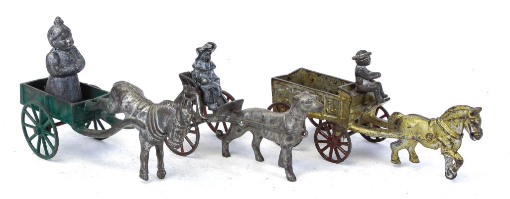THREE CAST IRON ANIMAL DRAWN CARRIAGES AND CARTS: American, 2nd quarter-20th century. Includes a dog pulled cart, 7" long, a horse pulled car with a mammy, 8" long, and a horse pulled coal cart with driver, 8.5" long.