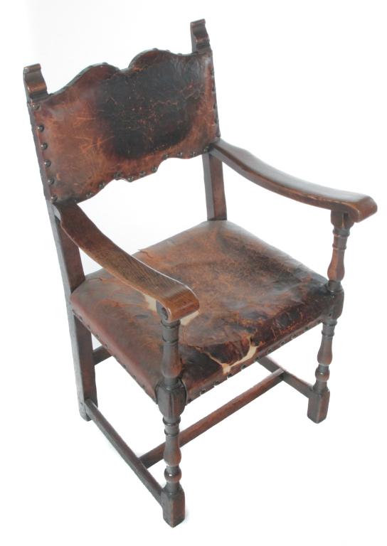 ENGLISH MEDIEVAL STYLE ARMCHAIR.: Late 19th-early 20th century, oak. Carved finials, turned front posts and leather upholstery. Loss to leather. 18" seat, 38"h.