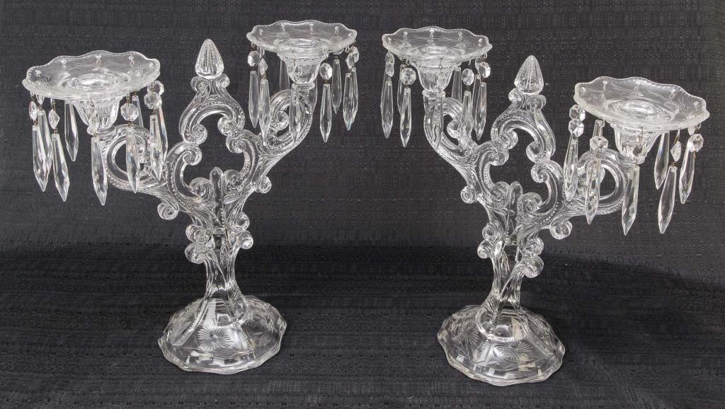 PAIR OF AMERICAN GLASS CANDELABRA.: Second quarter 20th century. Cut and pressed with scrolled branches with notched cutting, scalloped square bases with floral cutting, bobeche with vine cuttinga and prisms. Chips on two sockets. 13.5"