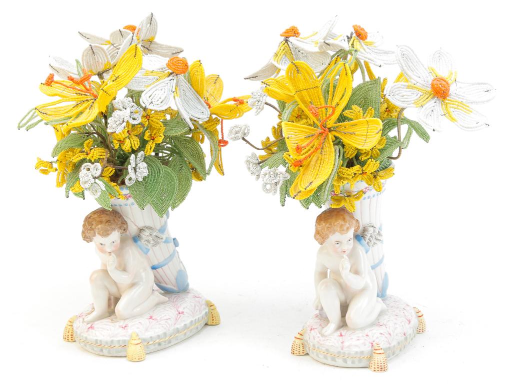 PAIR OF SITZENDORF PODET VASES.: German, late 19th century. Cherubs with quiver on tasseled cushion in muted colors. Double crossed lines mark, 6"h. With bouquets of beaded flowers.