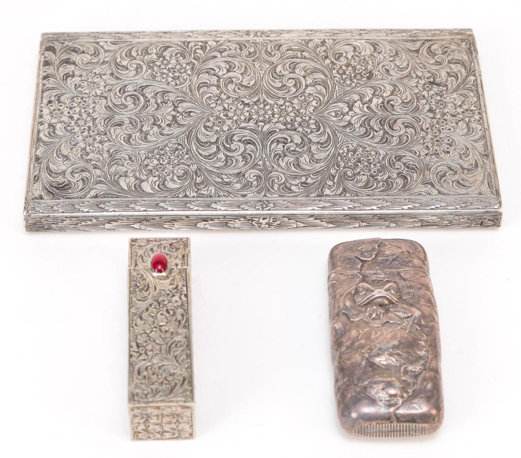 THREE PIECES OF SILVER.: Twentieth century. An 800 cigarette case with floral brightwork, 6"h. 3.25"w., and 800 lipstick case wit red cabochon bezel set stone clasp, 2.25"h. .75" sq. And a Shiebler sterling match safe with he