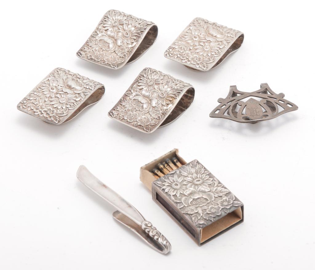 GROUP INCLUDING KIRK NAPKIN CLIPS.: Twentieth century. Four "S. Kirk & Son, Sterling" Repousse napkin clips and a match safe, 1.5"l. And two money clips "Sterling", and "South Seas Community". Sterling approx. 2.75 ozt.
