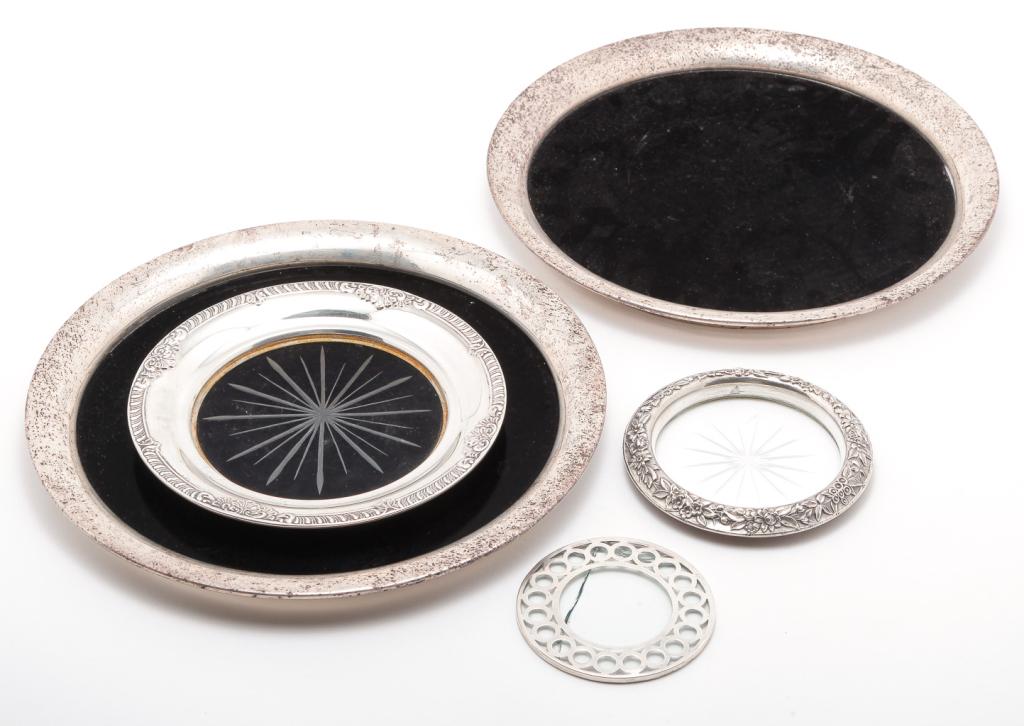 FOUR AMERICAN TRAYS AND COASTERS.: Twentieth century. "Sterling" overlay coaster (damaged), "S. Kirk & Son Sterling" rim bottle coaster, 4"d. And three silverplate rimmed trays. Pair with black plastic center, 9.5"d. and one glass, 6"d
