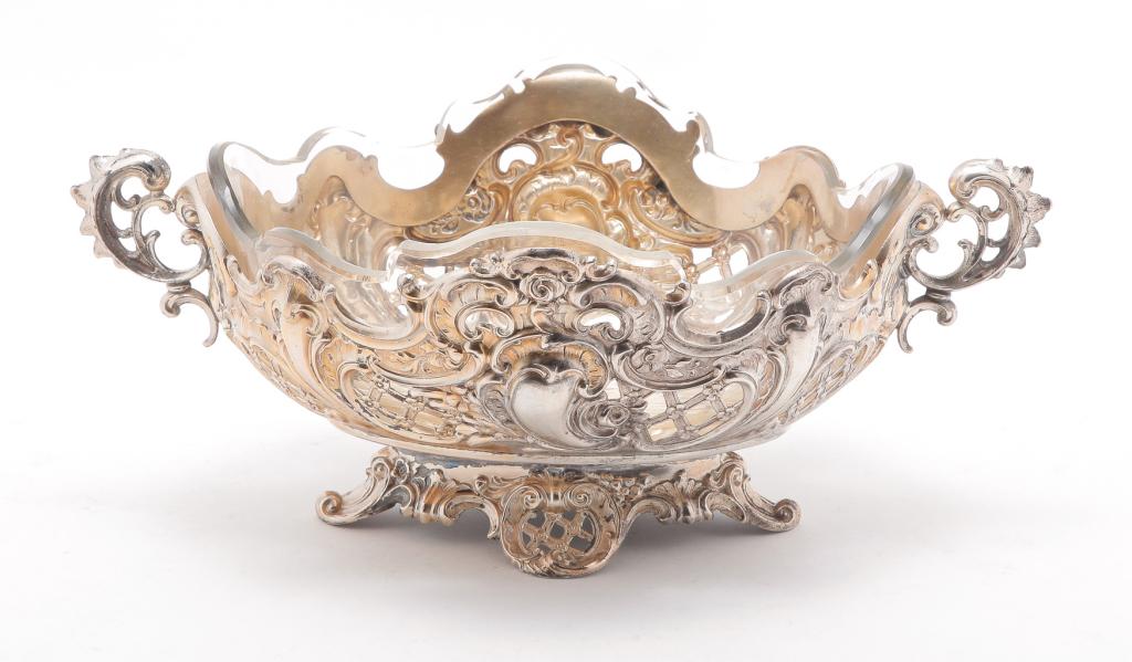 ROCOCO STYLE DISH WITH GLASS INSERT.: American or European, early 20th century. Pierce work dish with handles. Unmarked, most likely silverplate with some gold colored accents. Wear. 4"h. 9.75"l.