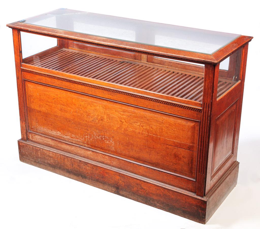 AMERICAN STORE COUNTER DISPLAY CASE.: Ca. 1900, oak. Fluted corners, raised panels, simple base moldings, two glass doors in back with lower storage and added cash drawer. Beveled glass top has been broken on one corner. 43"h. 60.5"w. 24.